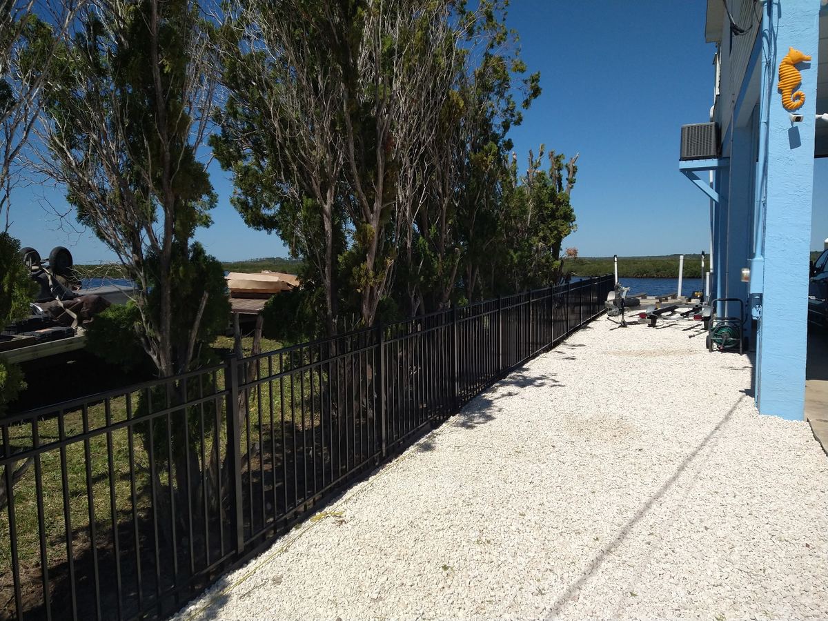 Black aluminum fence along a waterfront property with crushed shell walkway, installed by Florida Friendly Fencing