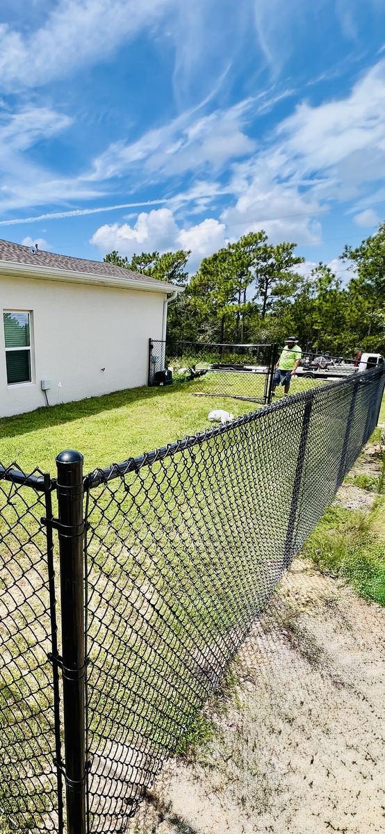 Black chain link fence and walk gate around a new home backyard with crew finishing installation, Florida