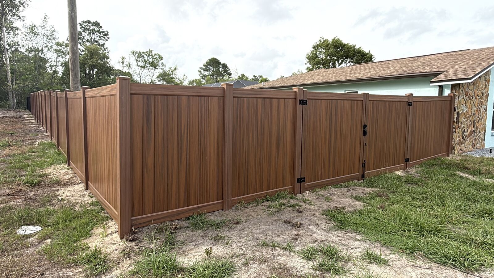 Mocha walnut wood-grain vinyl fence corner with gate hardware in Spring Hill FL