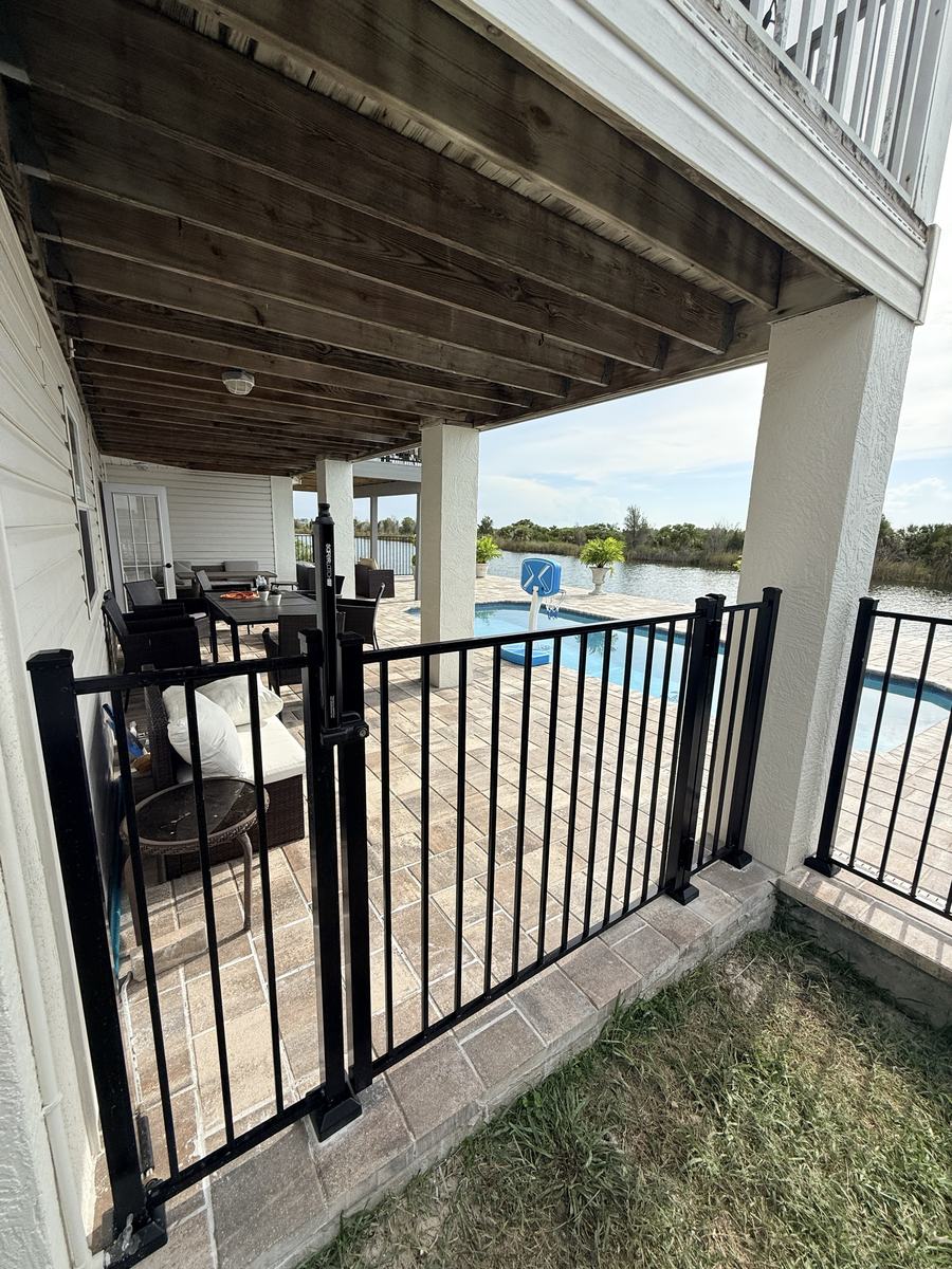 Self-closing black aluminum pool gate under a covered patio in Hernando Beach, FL