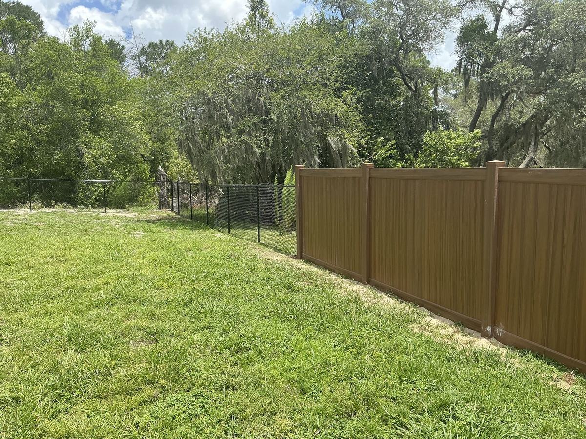 Mocha walnut vinyl privacy fence meeting black chain link in Spring Hill, FL